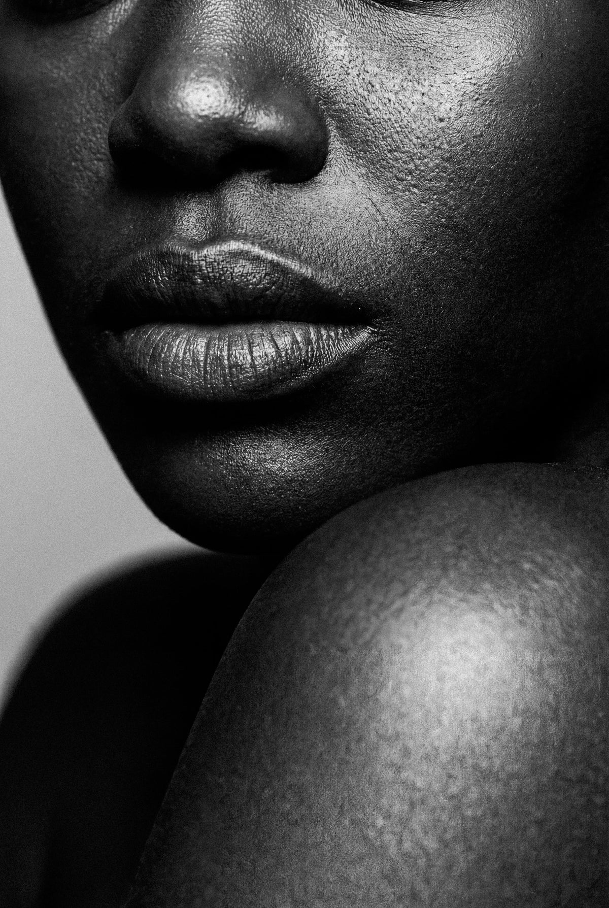Black and white close-up of a woman's lips, chin, and shoulder showing natural skin texture