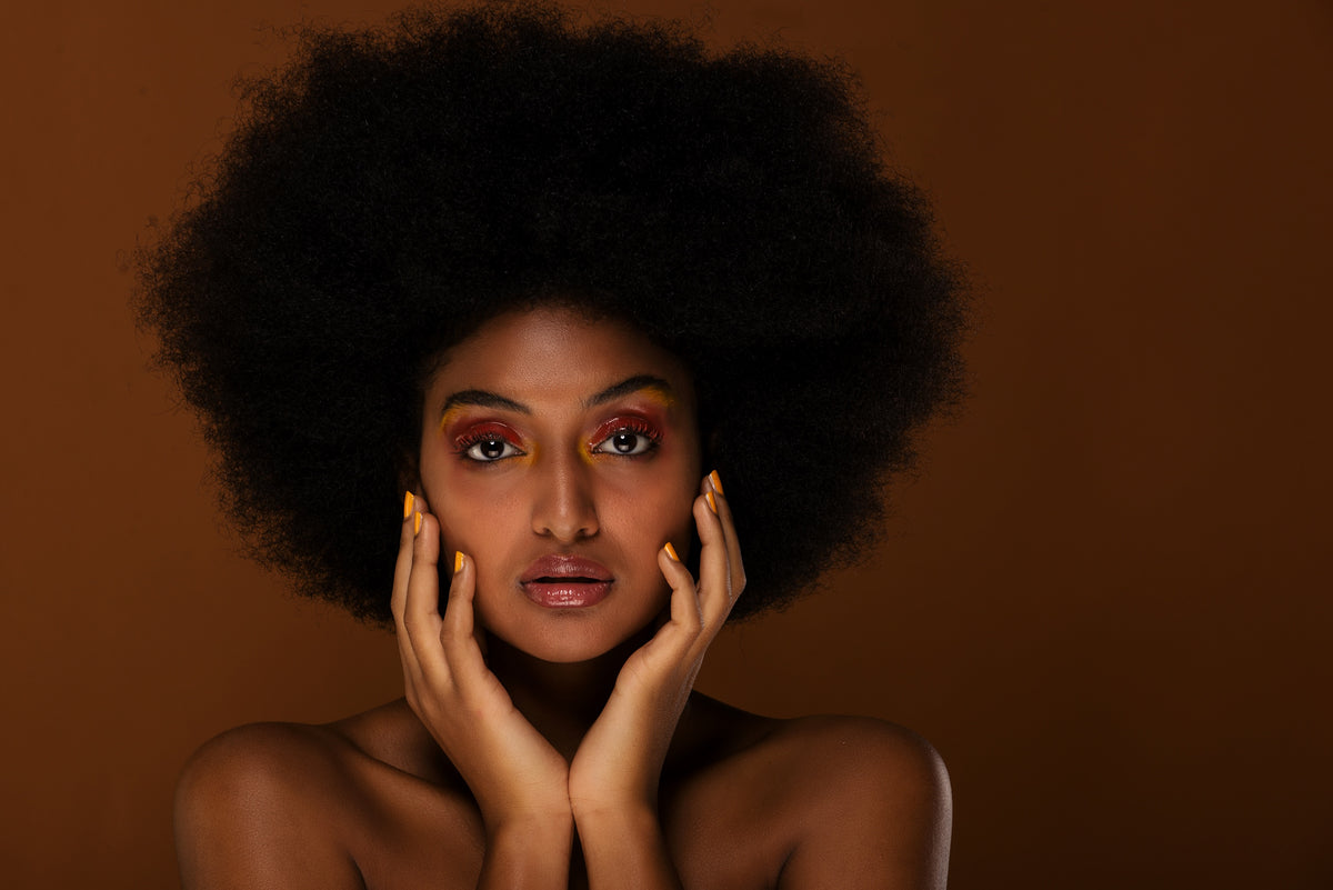 Woman with a full natural afro, hands framing her face, the textured hair Juje luxury scalp care is made for