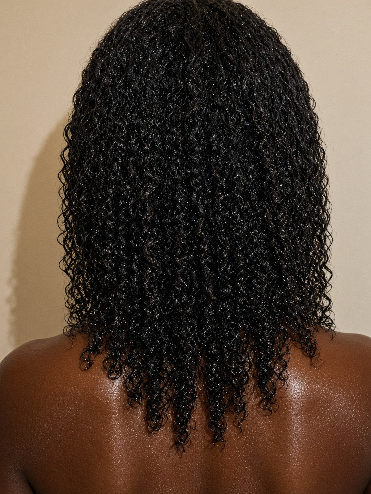 Back view of a woman with glossy, defined shoulder-length curls against a warm beige wall